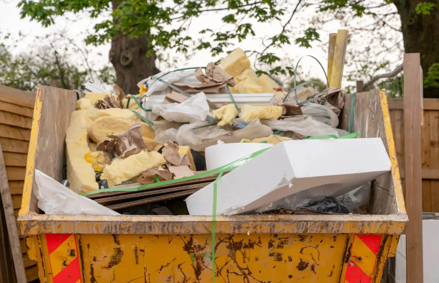 Yellow skip filled with bricks, cardboard, and rubble on a driveway, provided through professional skip hire Dorset by Dorset Skips