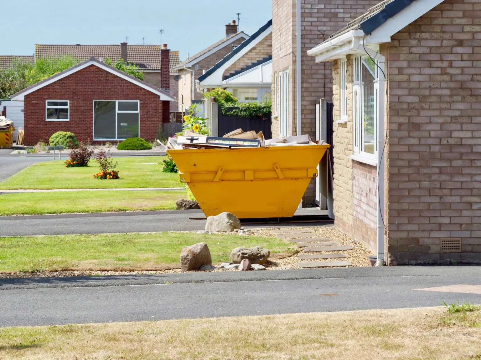 Yellow skip on a residential driveway beside a brick house, showcasing reliable domestic skip hire services from Dorset Skips